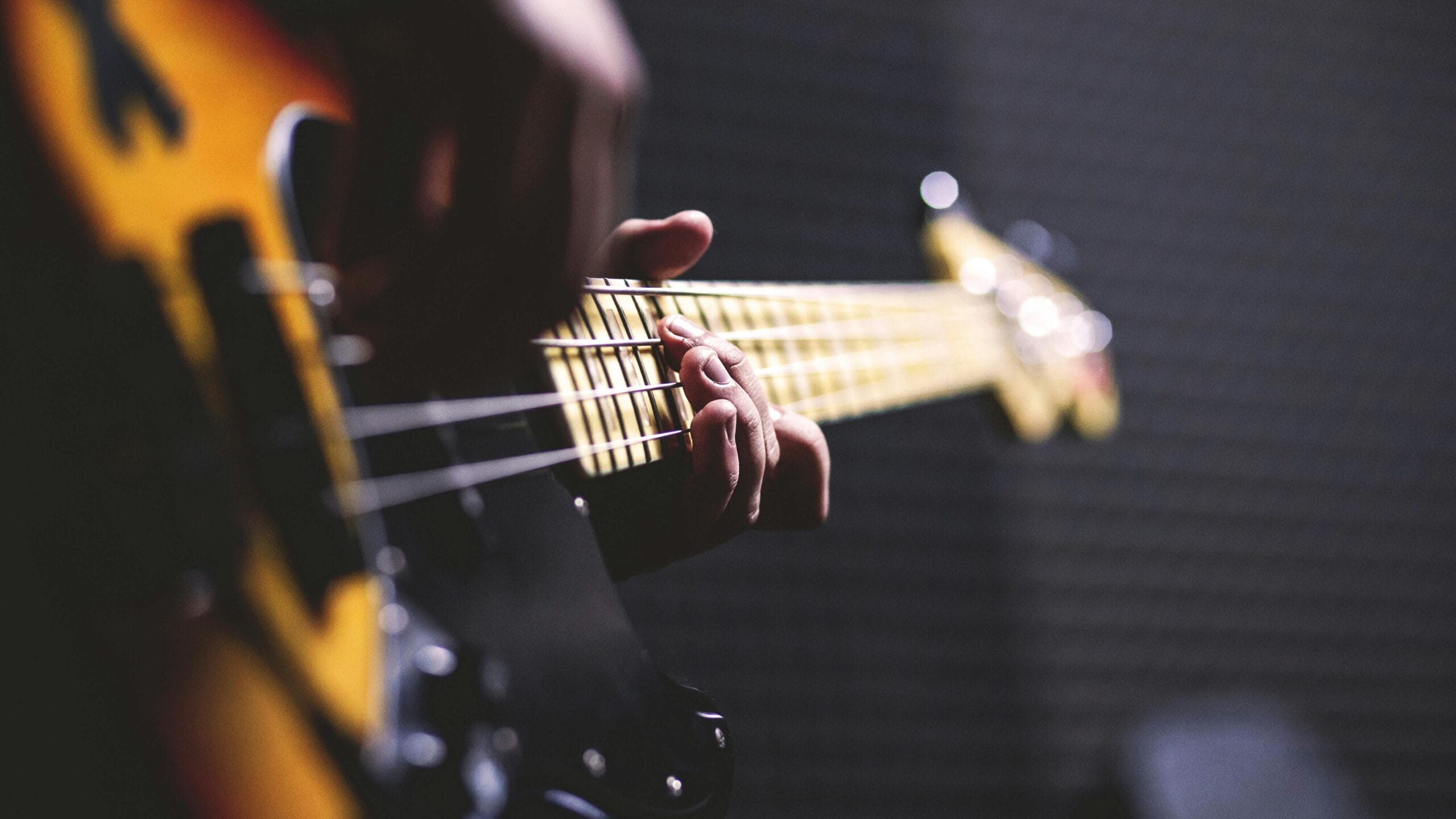 Contact Us Close-up of a musician strumming an electric bass guitar with focus on fingers.